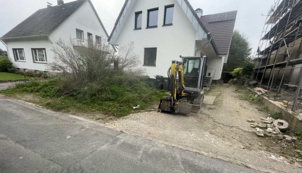 Minibagger beim Freiräumen einer Einfahrt vor einem Wohnhaus